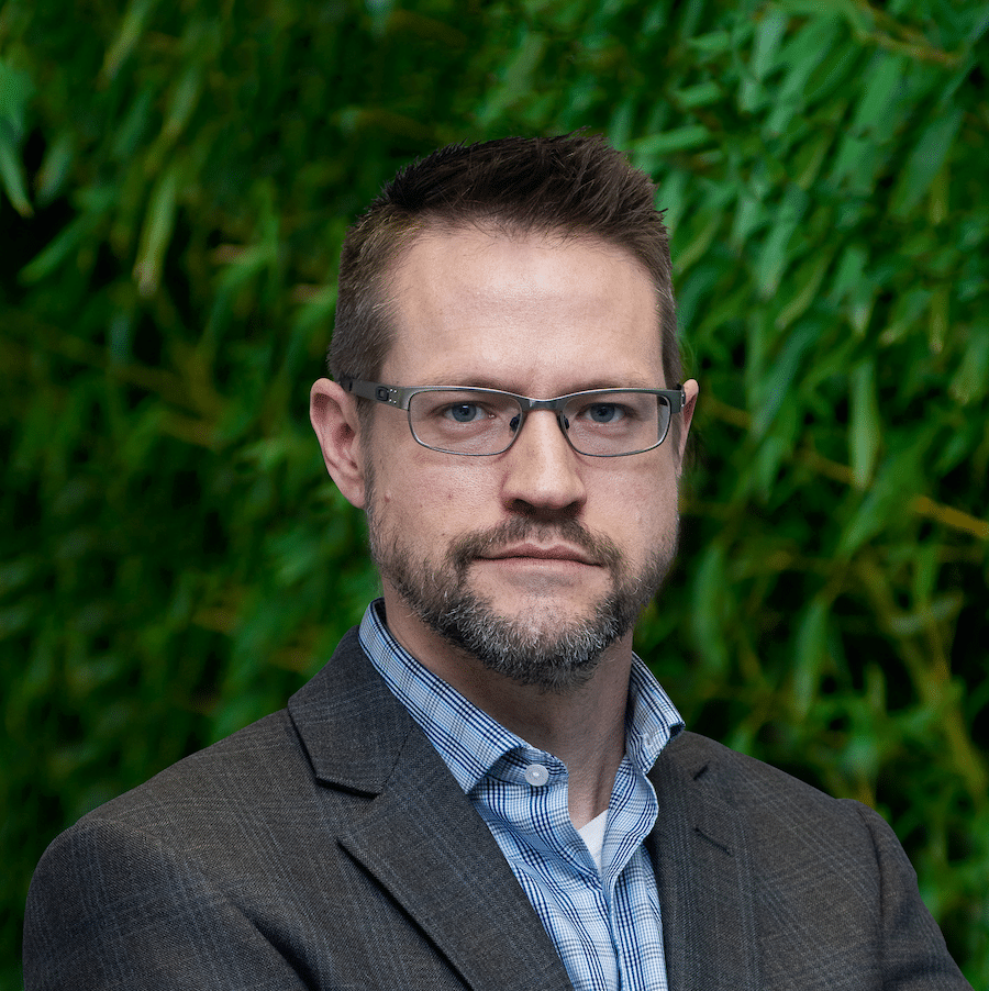 A man in glasses is standing in front of a green wall, offering strategic consulting.