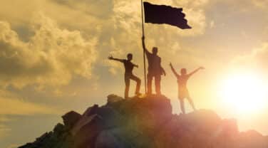 Three people standing on top of a mountain with an innovation flag.