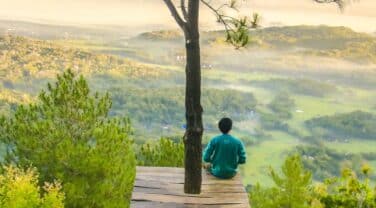 A man sits on a wooden platform overlooking a scenic valley, contemplating global innovation in consulting.