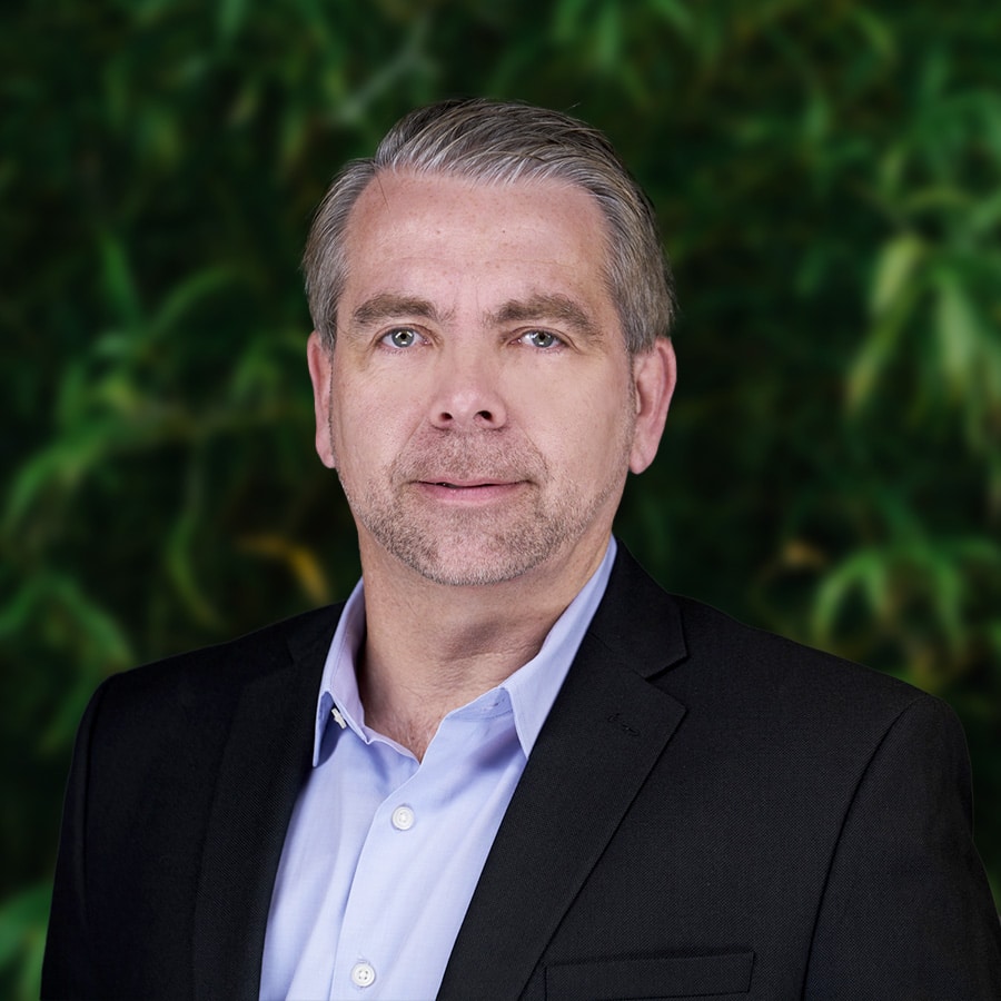 A man in a black suit standing in front of a green background, representing a strategic and tech-infused innovation in his presentation.