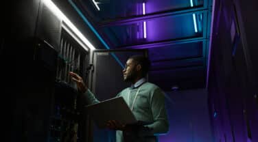 A global man in a server room looking at his laptop.