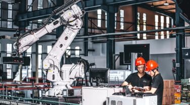 Two people collaborating with a robotic system in a factory, utilizing advanced technology.