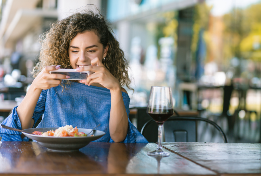 A woman strategically capturing her delicious food with the help of modern technology at a table.