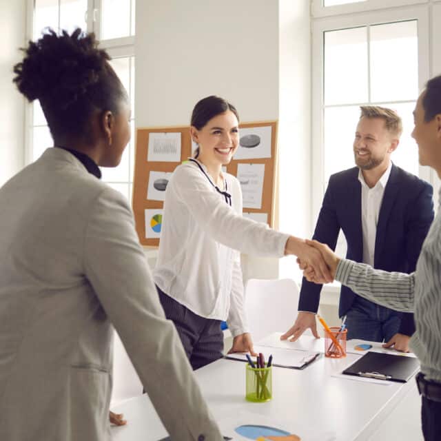 A group of strategic business people shaking hands in a tech-filled office.