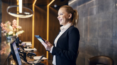 A happy receptionist is talking with hotel guest and making a reservation on a tablet.