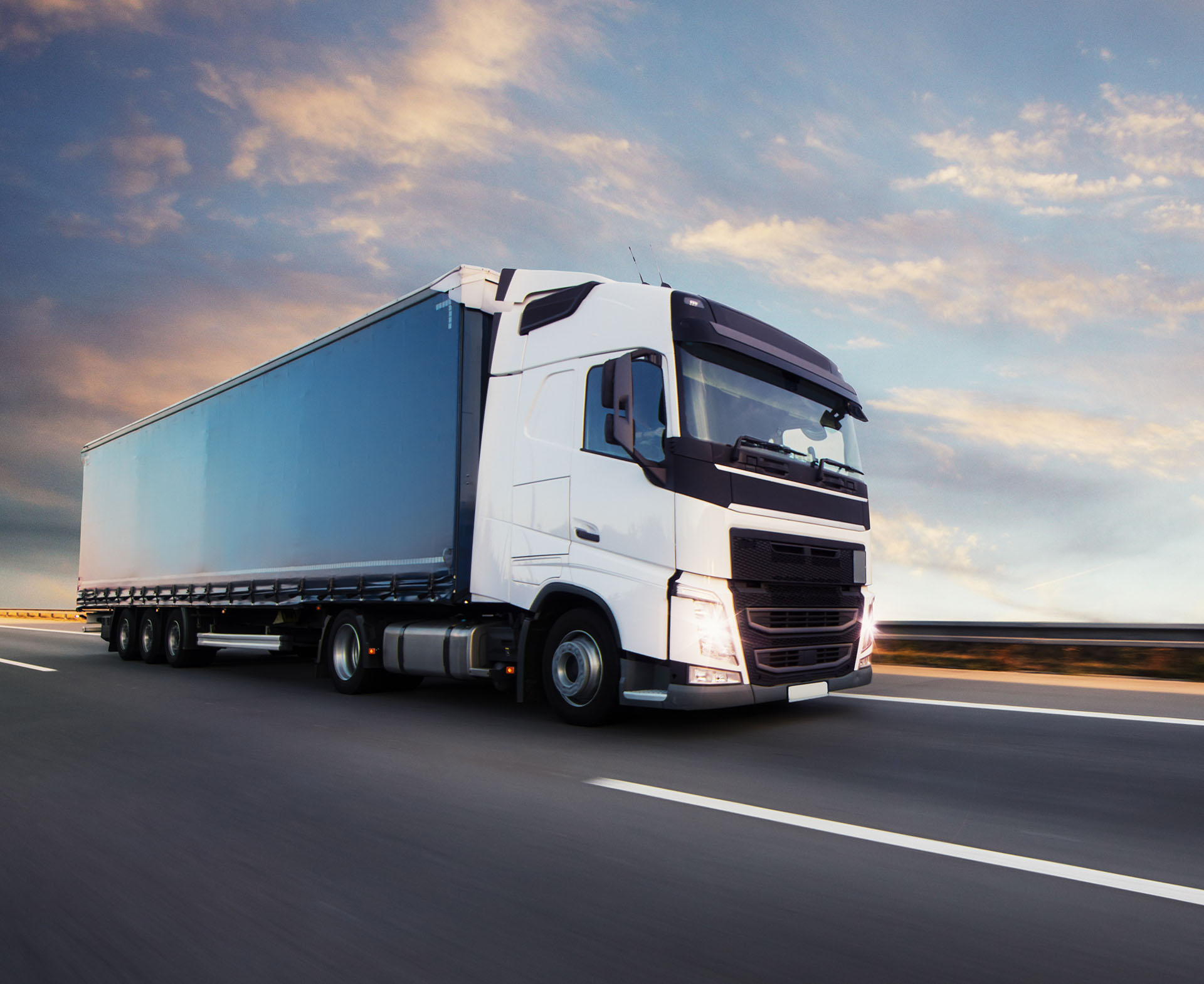 A semi truck driving on a highway at sunset.